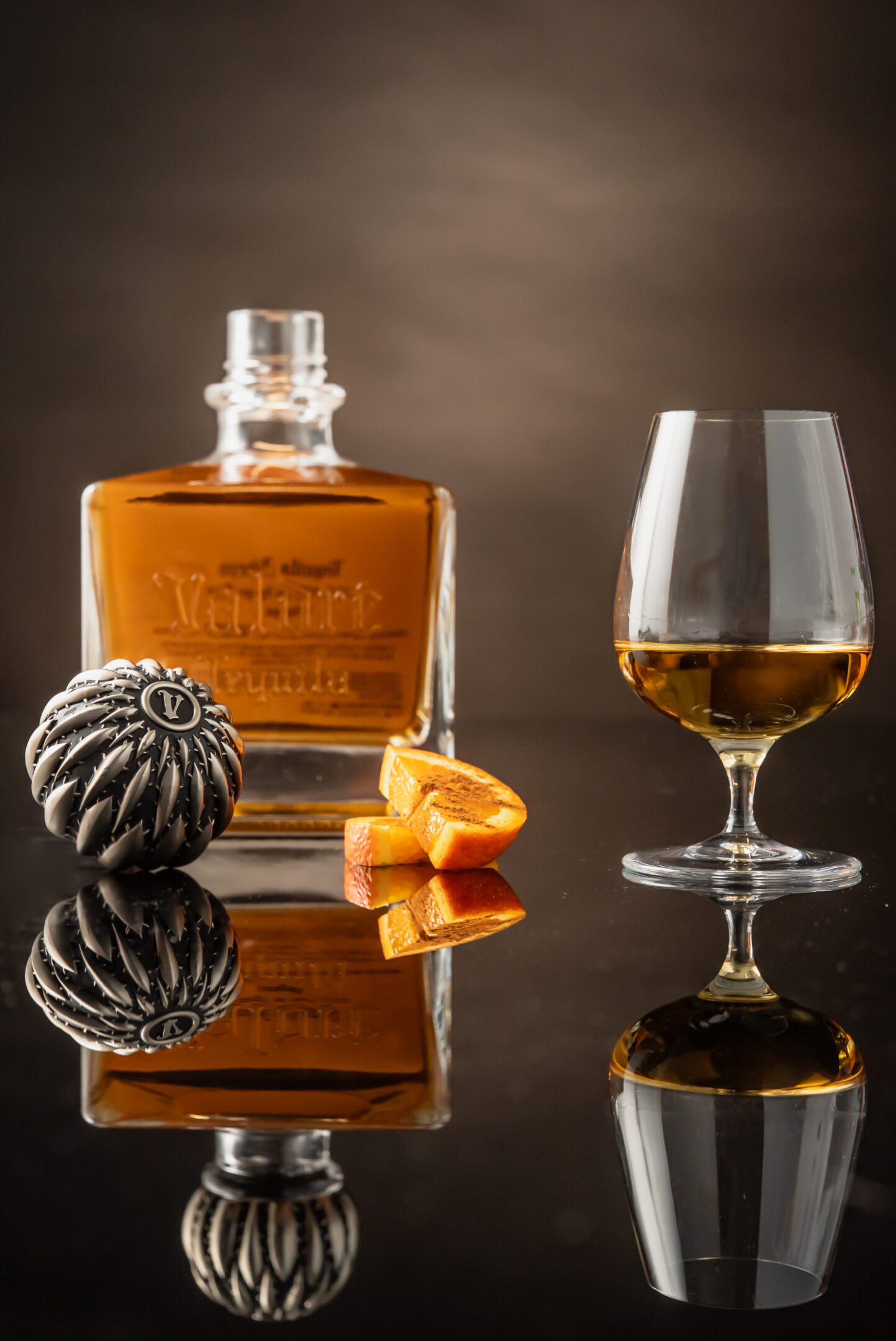 A glass of whiskey and an orange on the table.
